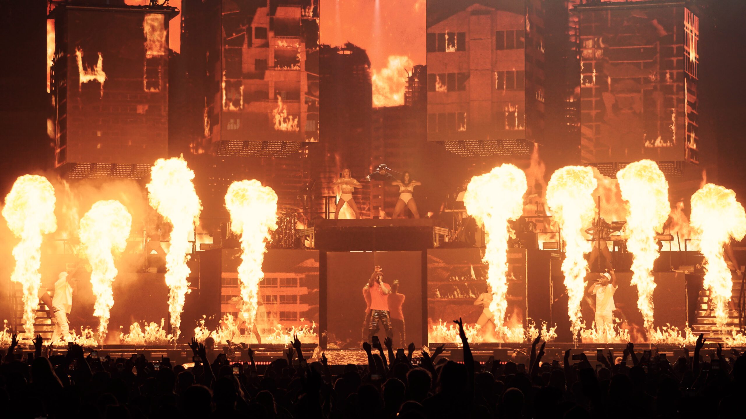 Pyro erupting across the stage in front of burning buildings on the screens