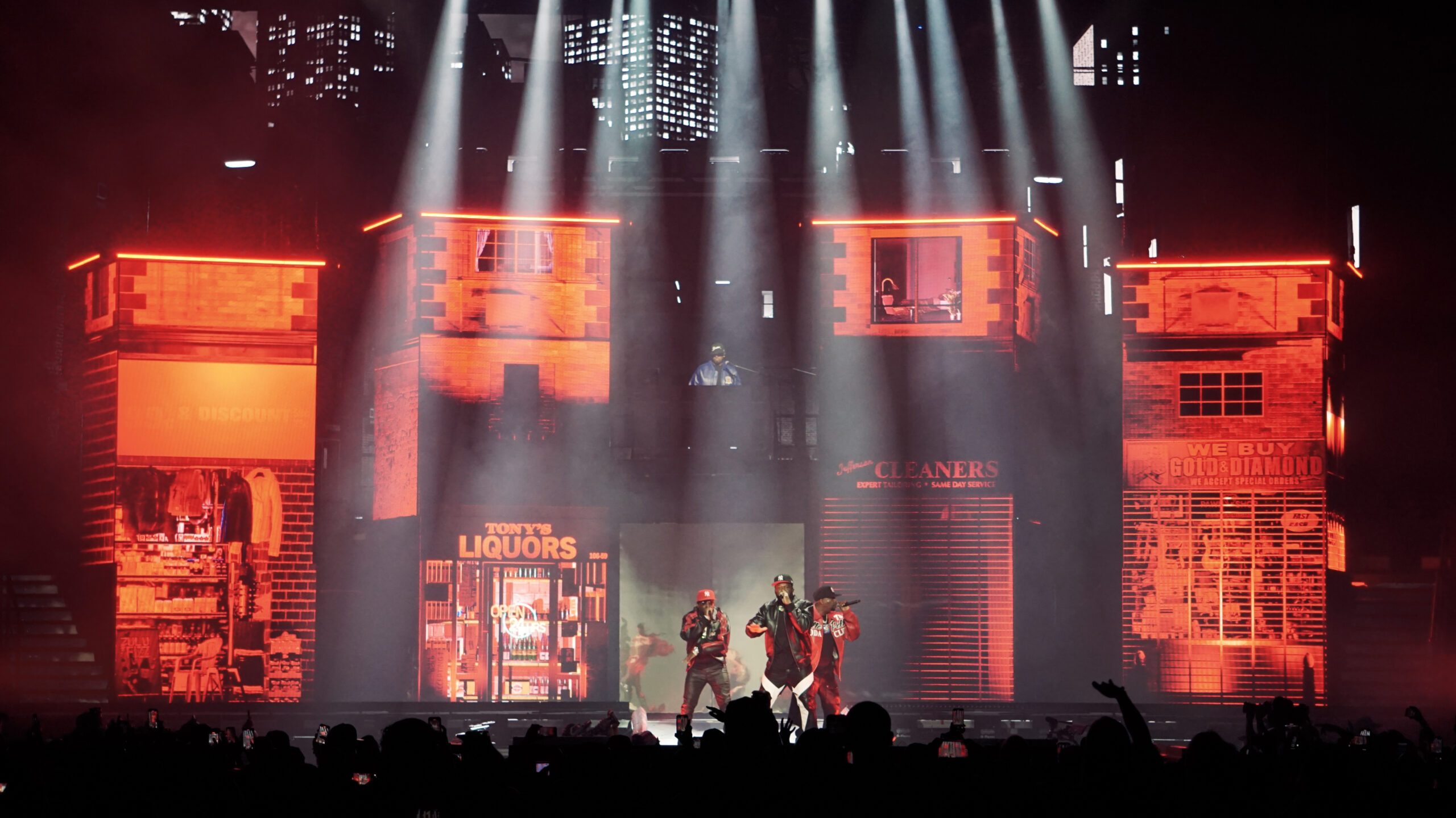 Glowing storefronts including Tony's Liquors, a cleaners and a gold buyer, as 50 Cent performs