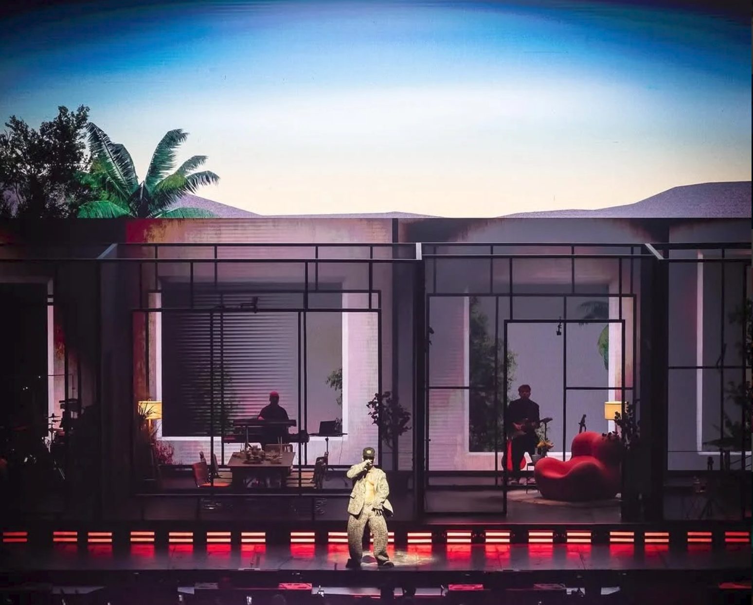 Manuel Turizo performing in front of the glass house under a dusk sky with palms