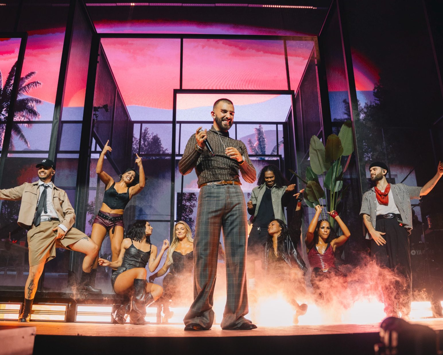 Manuel Turizo and dancers in front of a pink sunset and palm trees on the screens