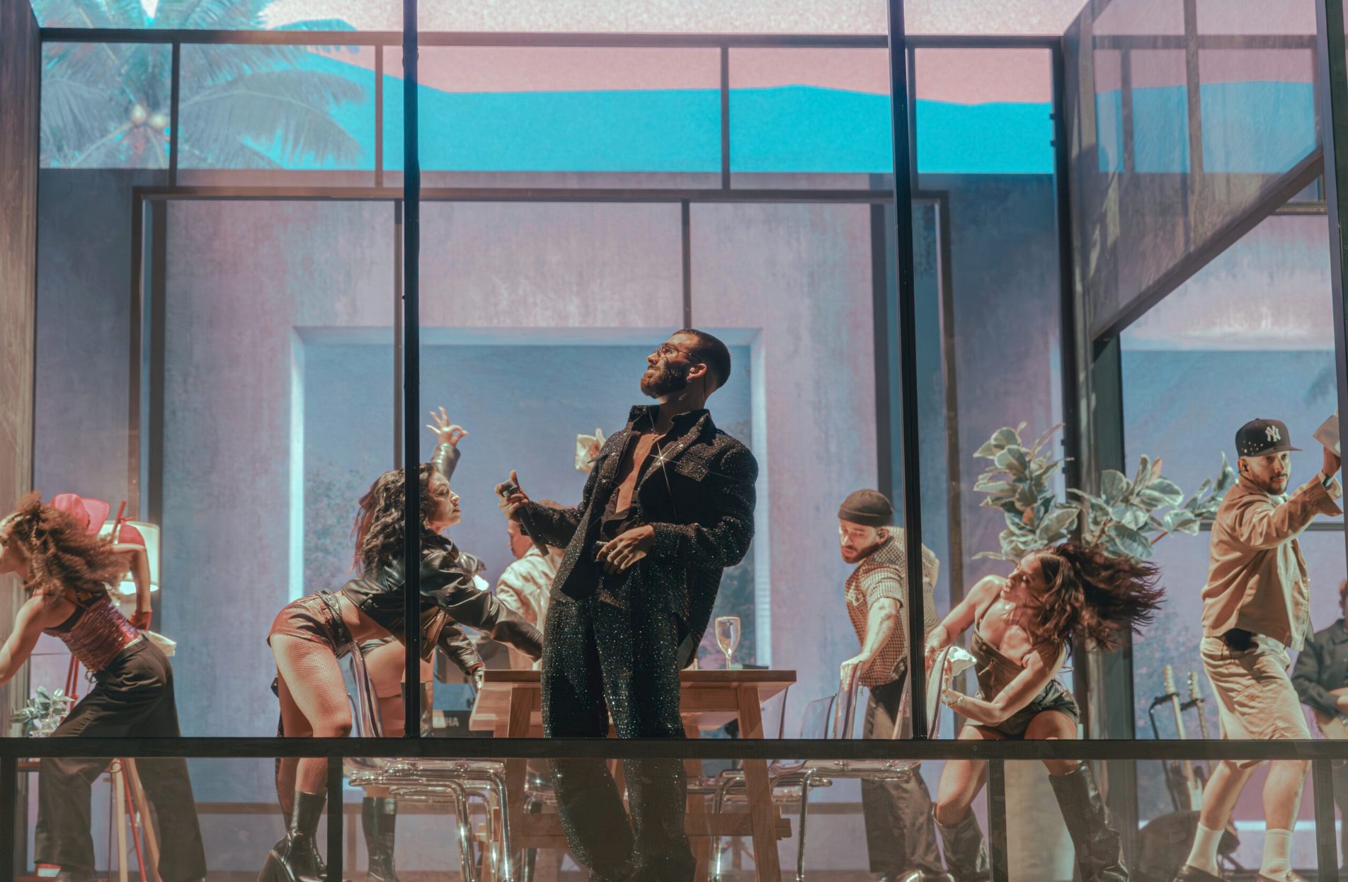 Manuel Turizo and dancers inside the glass house against a pastel blue sky